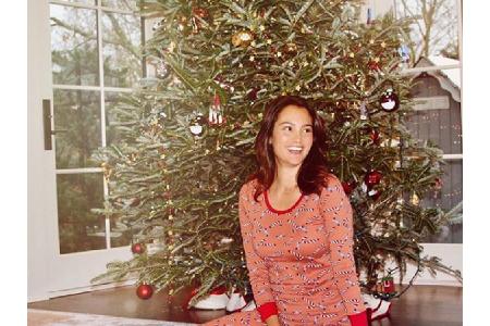 Model Emma Heming macht es sich in ihrem Pyjama vor dem Weihnachtsbaum gemütlich.