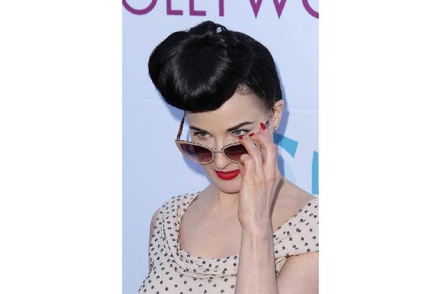 ...dass Burleske-Star Dita Von Teese so gekonnt über ihre Sonnenbrille blickt wie sie sich im großen Champagnerglas räkelt.