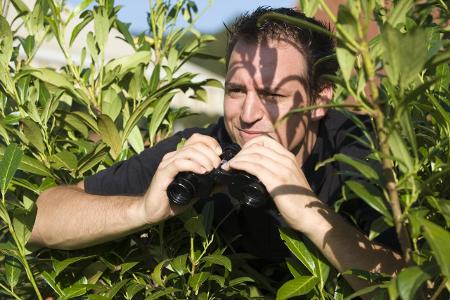 Neugieriger Nachbar mit Fernglas versteckt sich hinter der H...