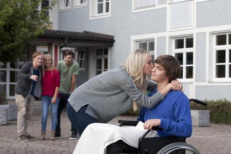 Young woman kissing her boyfriend sitting in wheelchair mode...