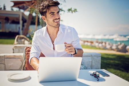 Mann vor dem Computer sitzend mit Handy und Sonnenbrille