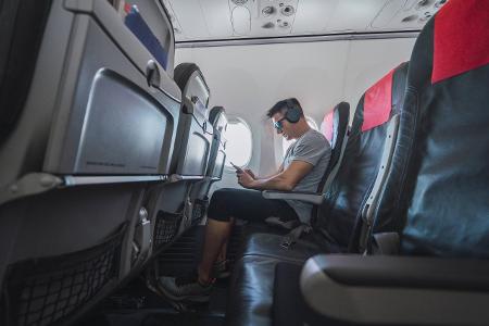 Man in airplane, using smartphone, headphones model released...