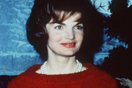 Knallrotes Kostüm mit Perlenkette: Jackie Kennedy bei einem Pressetermin