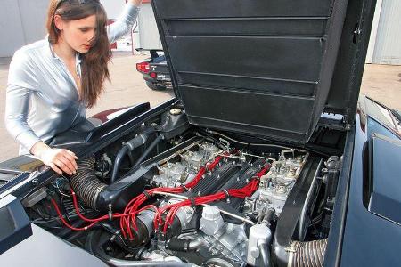 Brünette im silbernen Catsuit blickt auf den V12-Motor des Lamborghini Countach LP 400