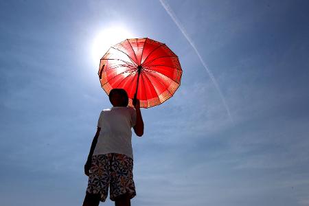 HOT WEATHER ADELAIDE, A man walks with an umbrella at Henley...