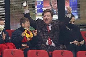 Edelfan Elton John jubelt im Fußballstadion mit Anzug und Krawatte