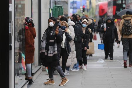 Menschen stehen in London mit Maske vor geöffneten Geschäften