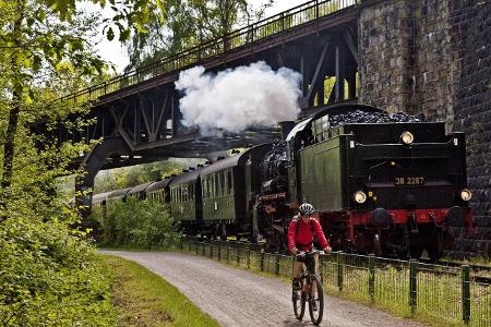 Fahrradfahrer auf dem Ruhrtalradweg mit der historischen Dam...