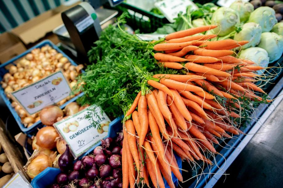 Karotten und Zwiebeln stehen an einem Obst- und Gemüsestand auf einem Wochenmarkt zum Verkauf.