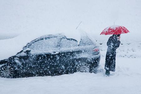 woman on mobile alongside car in a snow drift