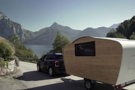 Der Teardrop-Caravan Free Chilli hängt an einem Zugfahrzeug. Im Hintergrund ist ein See zu sehen, der von einem Gebirge eingerahmt wird.