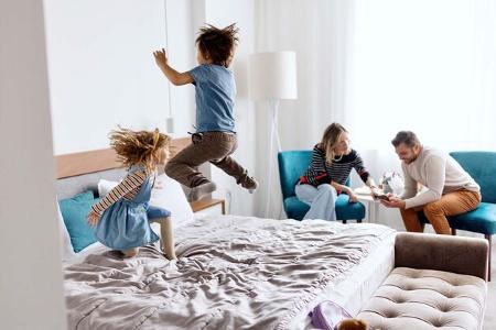Brother and sister playing and jumping on the bed in the hotel room