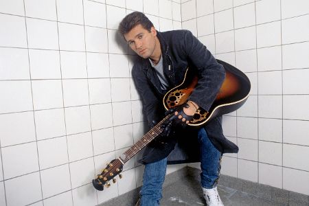 Mann mit Gitarre hockt in der Ecke eines gefliesten Raumes