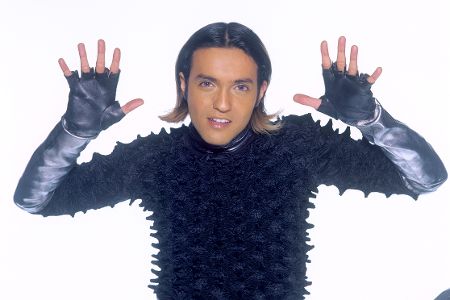 Mann mit halblangen Haaren und spickiger Jacke hält die Hände hoch