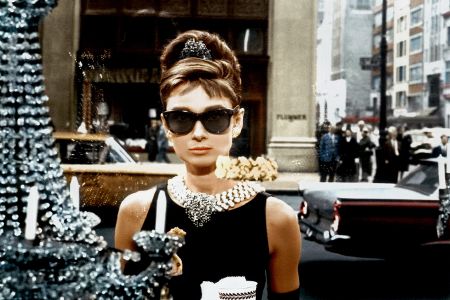 Frau mit Sonnenbrille steht vor einem Schaufenster mit einem Kronleuchter.