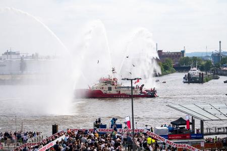 Ein Feuerlöschboot fährt an den Landungsbrücken mit Wasserfontänen entlang.