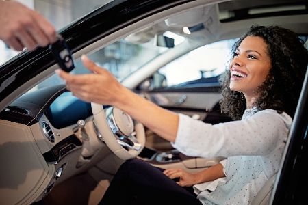 Frau sitzt im Auto und bekommt den Schlüssel