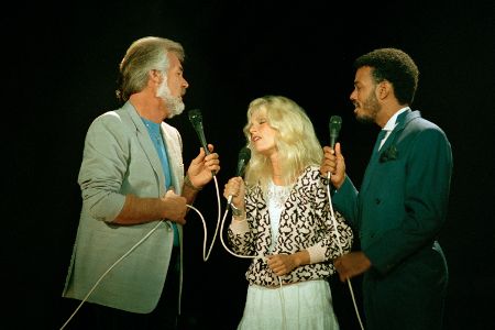 Zwei Männer und eine Frau stehen mit Mikrofonen auf einer Bühne und singen gemeinsam.