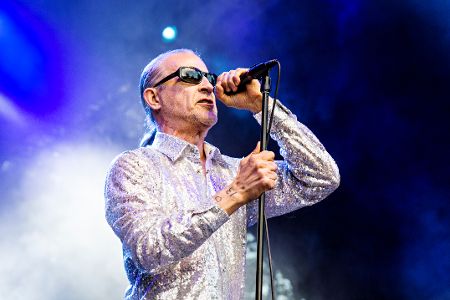 Mann mit Zopf und Sonnenbrille steht vor einem Mikrofon und singt.