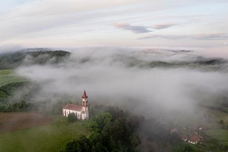 Morgennebel steigt über der Herz-Jesu-Kirche im ungarischen Soshartyan auf.