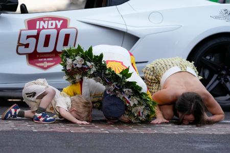 Josef Newgarden (M.) küsst gemeinsam mit seinem Sohn Kota und seiner Frau Ashley Welch den Boden, nachdem er das Indianapolis 500 Autorennen auf dem Indianapolis Motor Speedway gewonnen hat.