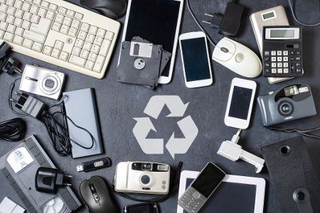 Alte Elektrogeräte liegen auf einem Tisch um das Recyclingsymbol herum.