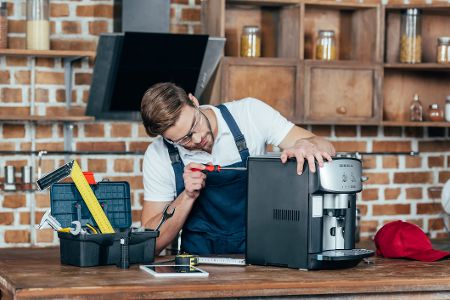 Mann steht in einer Küche und baut an einem Kaffeevollautomaten herum