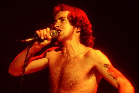 Mann mit freiem Oberkörper singt ins Mikrofon