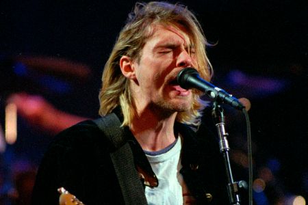 Mann mit langen Haaren und Gitarre singt auf einer Bühne