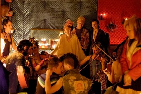 Szene in einem Club mit vielen Menschen, Musikern und Personen, die sich küssen