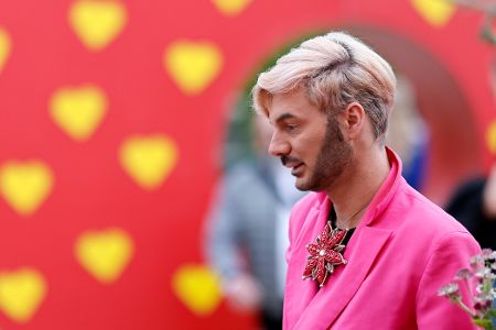Mann mit rosa Shirt und Bart vor rotem Hintergrund mit gelben Herzen