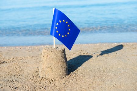 Sandburg mit EU-Flagge vor Gewässer
