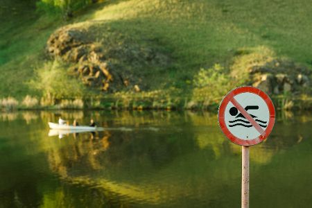 Badeverbotsschild vor einem Gewässer, auf dem ein Boot fährt