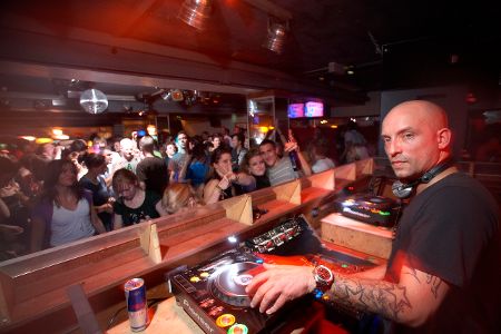 DJ am Pult vor feiernder Menge schaut in die Kamera