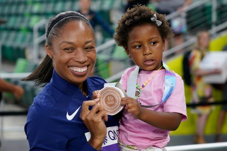 Sportlerin mit Kind auf dem Arm und Medaille in der Hand