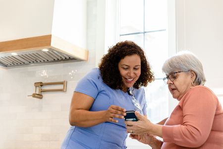 Pflegekraft hilft seniorin mit handy