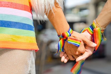 Zwei Menschen mit Regenbogenbändern am Armgelenkt fassen sich an den Händen Zwei Menschen mit Regenbogenbändern am Armgelenkt fassen sich an den Händen
