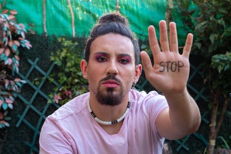 Mann mit Lippenstift und langen Haaren hebt seine Hand, auf der Stop geschrieben steht