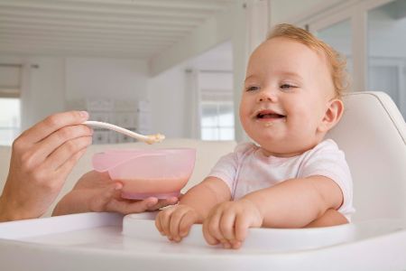 Baby im Hochstuhl wird gefüttert