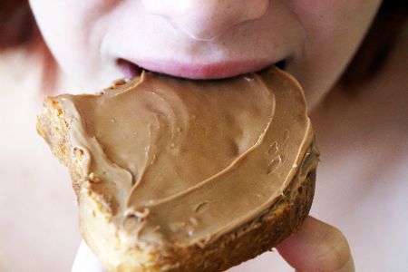 Mensch beißt in ein Brot, das mit Erdnussbutter belegt ist
