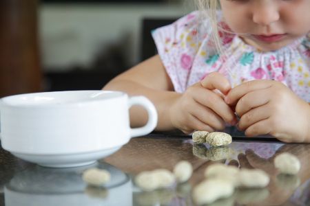 Kleines Mädchen sitzt vor einer Schüssel mit Erdnüssen