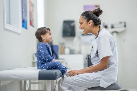 Kind sitzt im Krankenhaus auf einem Bett, davor hockt eine Krankenschwester