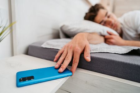 Mann im Bett tastet nach seinem Handy auf dem Nachttisch