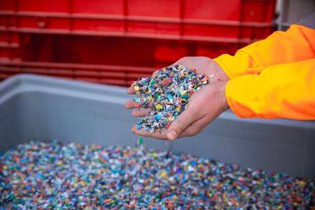 Hände greifen in Container voll mit geschredderten Plastikteilchen