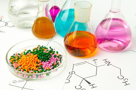 Reagenzgläser mit bunten Flüssigkeiten vor Schälchen mit kleinen Plastikstückchen