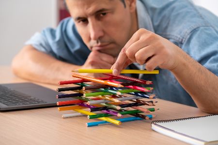 Mann baut gelangweilt stapel aus Buntstiften