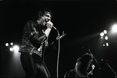 Paul Di'Anno, Sänger von Iron Maiden in Lederkluft auf einer Bühne am Singen.