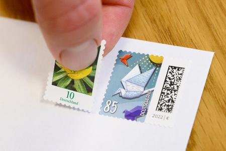 Eine 10-Cent-Briefmarke wird neben eine 85-Cent-Briefmarke geklebt (gestellte Szene). 