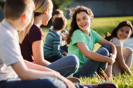 Jungen und Mädchen sitzen auf einer Wiese und unterhalten sich