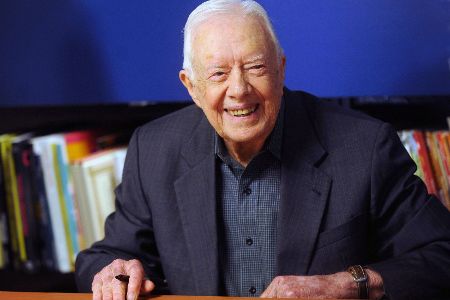 Jimmy Carter sitzt an einem Tisch und lächelt in die Kamera.